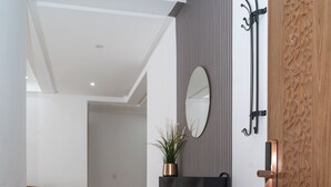 Un couloir avec une porte en bois, un meuble noir fixé au mur, un miroir et une plante.