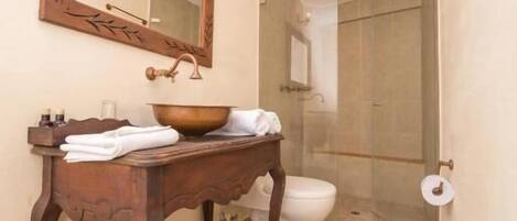 A bathroom with a wooden vanity, a large mirror, a sink, a toilet, and a shower area.