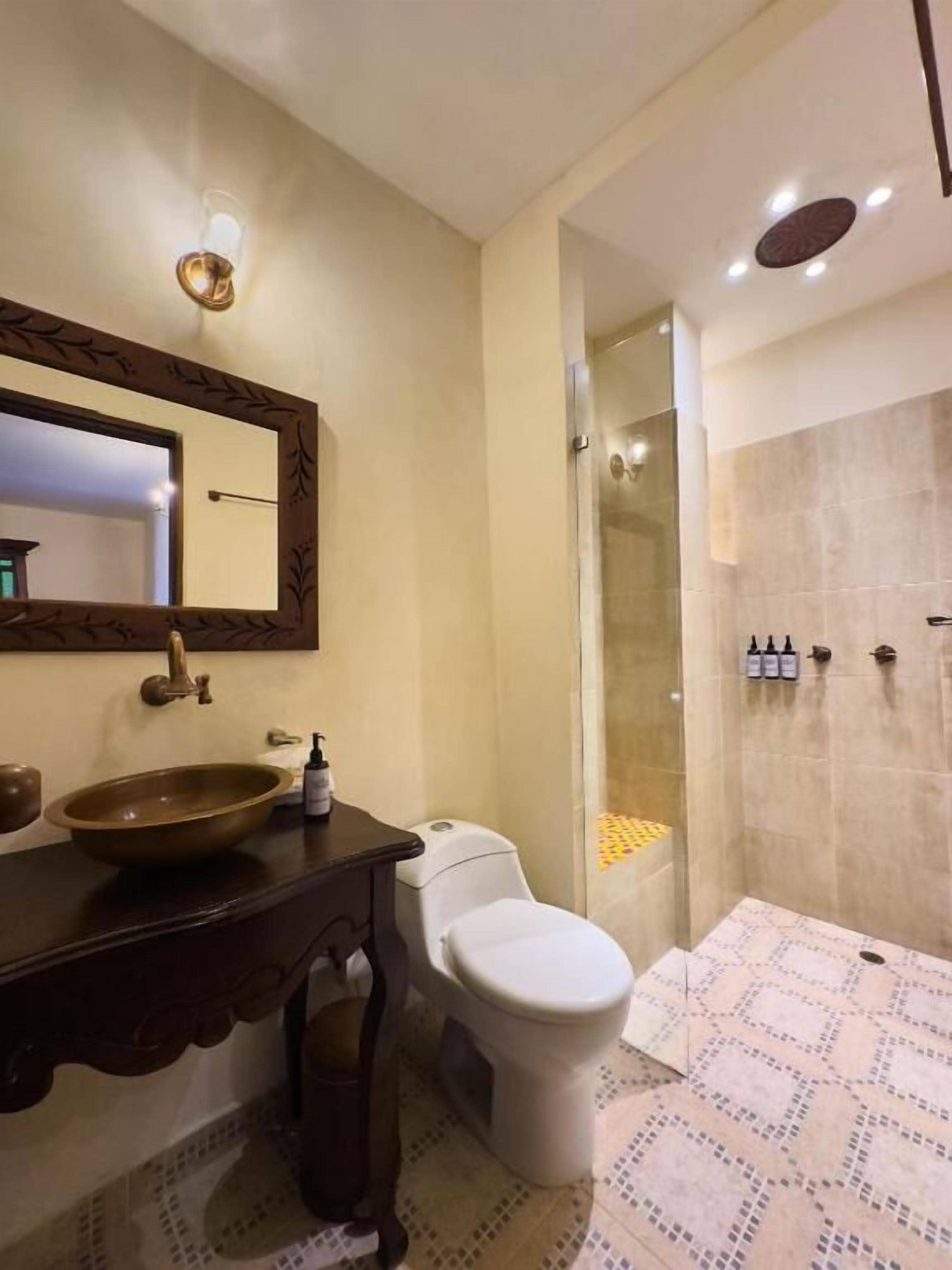 Un baño con un lavamanos redondo, un inodoro, una ducha y un espejo con diseño de hojas.