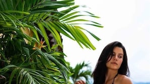 Eine Person in einem schwarzen Bikini am Pool mit Blick auf Grünflächen und ein Gewässer.