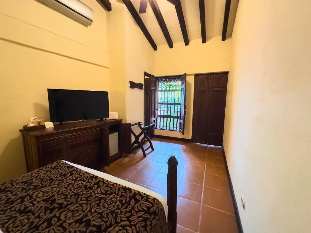 A bedroom with a bed, a desk, a chair, a TV, a wardrobe, and a balcony with a view.