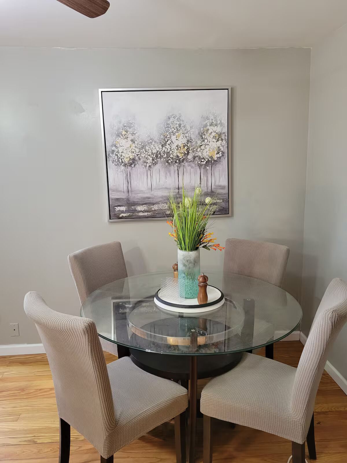 Un coin repas avec une table en verre entourée de quatre chaises rembourrées. Un vase rempli de fleurs est posé sur la table.