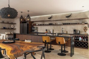 A modern kitchen with a wooden dining table, bar stools, and a wine rack. - Casa Natura, Private Plunge w Bikes (Tulum)