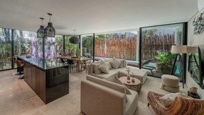 Un intérieur moderne avec un îlot central, un coin salon et de grandes fenêtres offrant une vue sur la verdure.