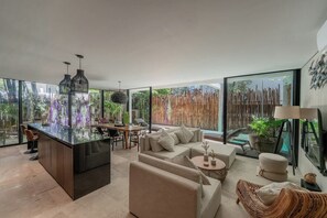 A modern interior with a central island, seating area, and large windows offering views of greenery. - Casa Natura, Private Plunge w Bikes (Tulum)