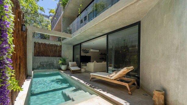 Un espace piscine extérieur moderne, doté de chaises longues, d’un petit coin salon et d’un espace clos par des parois de verre.