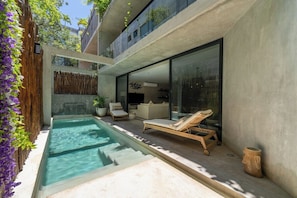 A modern outdoor pool area with lounge chairs, a small seating area, and a glass-enclosed space. - Casa Natura, Private Plunge w Bikes (Tulum)