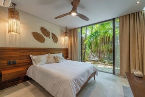 A bedroom with a large bed, a ceiling fan, a wall-mounted light, and a view of greenery outside. - Casa Natura, Private Plunge w Bikes (Tulum)