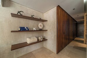 A hallway with wooden shelves displaying various items, a textured wall, and a wooden panel on the right. - Casa Natura, Private Plunge w Bikes (Tulum)
