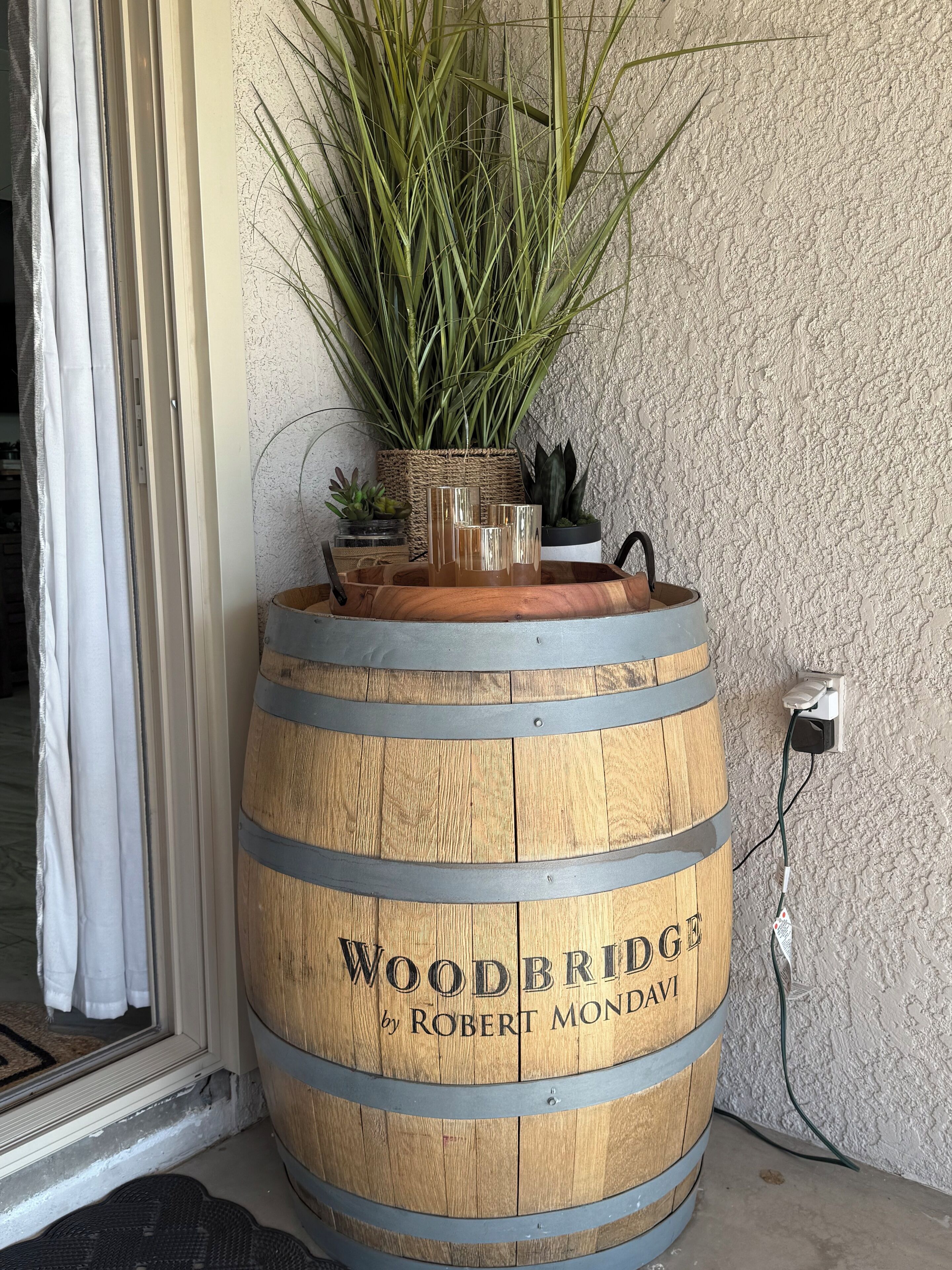 A wooden barrel with the text "WOODBRIDGE by ROBERT MONDAVI" and a potted plant on top.