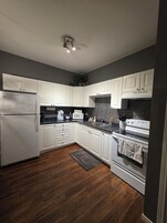 A modern kitchen with white cabinets, a black countertop, a stainless steel refrigerator, a microwave, and an oven.
