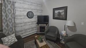 Una sala de estar con chimenea, televisor y un cuadro en la pared.