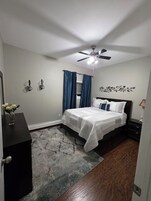 A bedroom with a bed, a ceiling fan, a nightstand, a dresser, and a decorative wall piece.