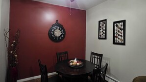 Comedor con una mesa redonda, cuatro sillas, un ventilador de techo, un reloj de pared y dos adornos enmarcados.
