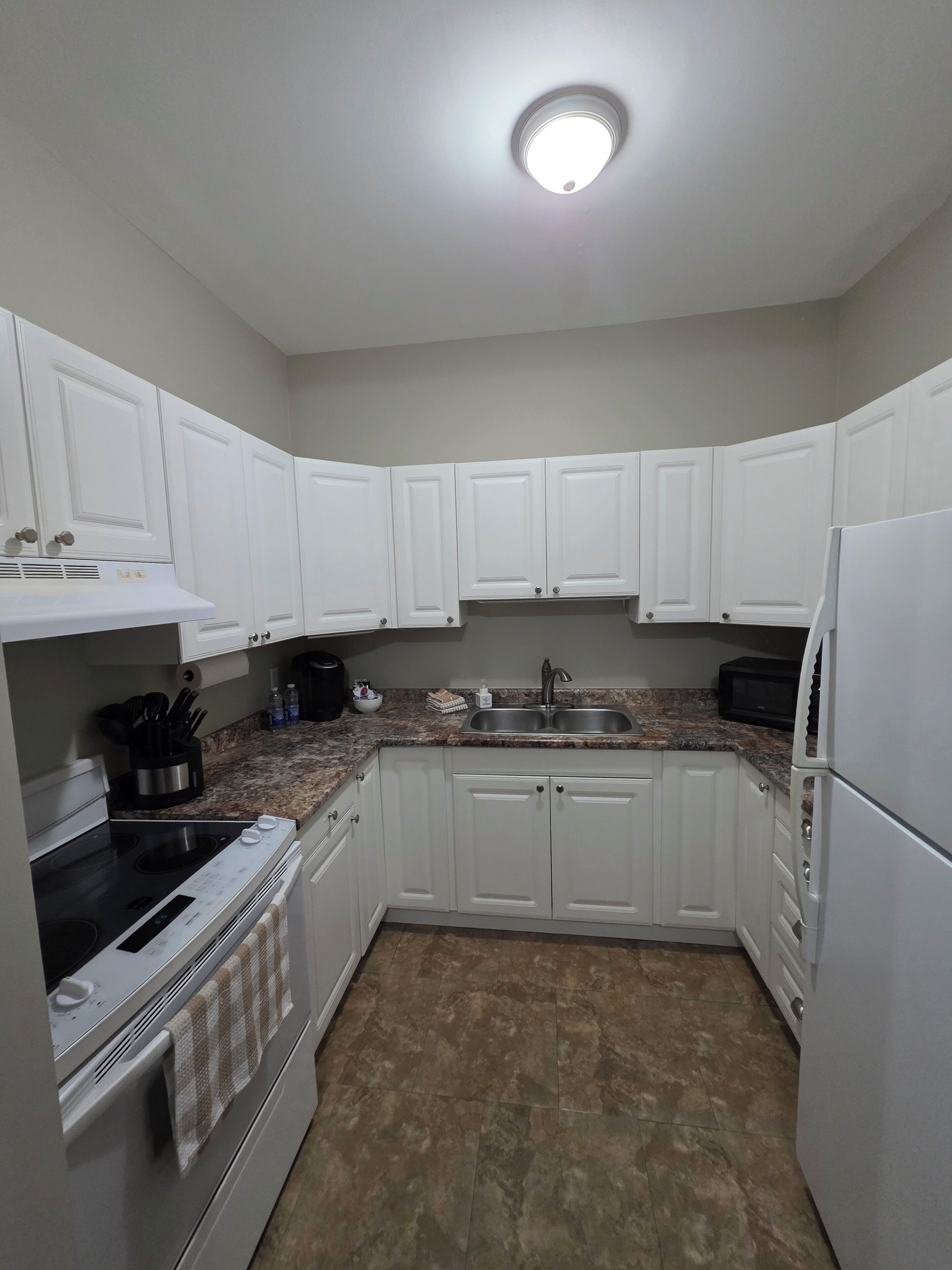 A kitchen with white cabinets, a granite countertop, a stainless steel sink, a stove, and a refrigerator.