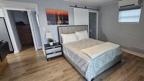 Un dormitorio con cama, mesitas de noche, cómoda, ventana con persianas y aire acondicionado de pared.