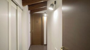 A narrow hallway with white walls and a wooden ceiling. A door with a light fixture above it is visible at the end of the hallway. - Casa Soele your home away from home (Pontecagnano)
