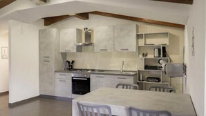 A modern kitchen with grey cabinets, a built-in oven, and a dining area with a table and chairs. - Casa Soele your home away from home (Pontecagnano)