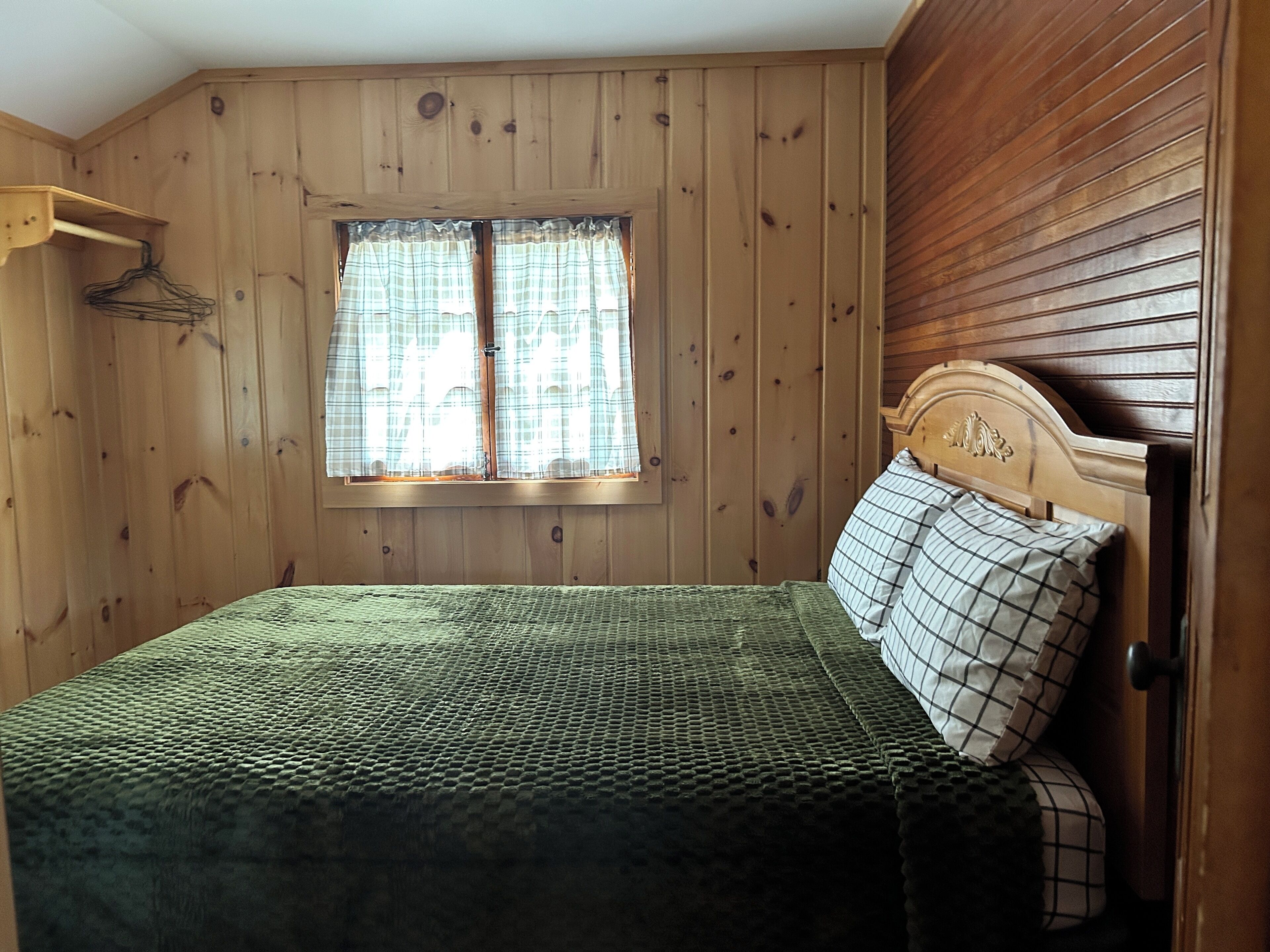 A wooden room with a bed, a window with curtains, and a wooden headboard.