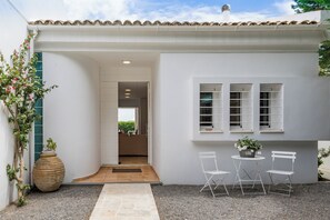 Un edifici blanc amb teulada de rajola, un petit pati amb taula i cadires, i una gran jardiniera amb flors.