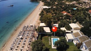 An aerial view of a coastal area with a beach, a row of sun loungers, and a swimming pool surrounded by buildings. - Villa Piedra, Seafront 3 Bedroom Villa with Direct Beach Access - Barbati, Corfu (Mparmpati)
