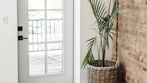 Une porte d’entrée avec une porte blanche, un panier en osier contenant une plante et un tapis à motifs posé sur un plancher en bois.