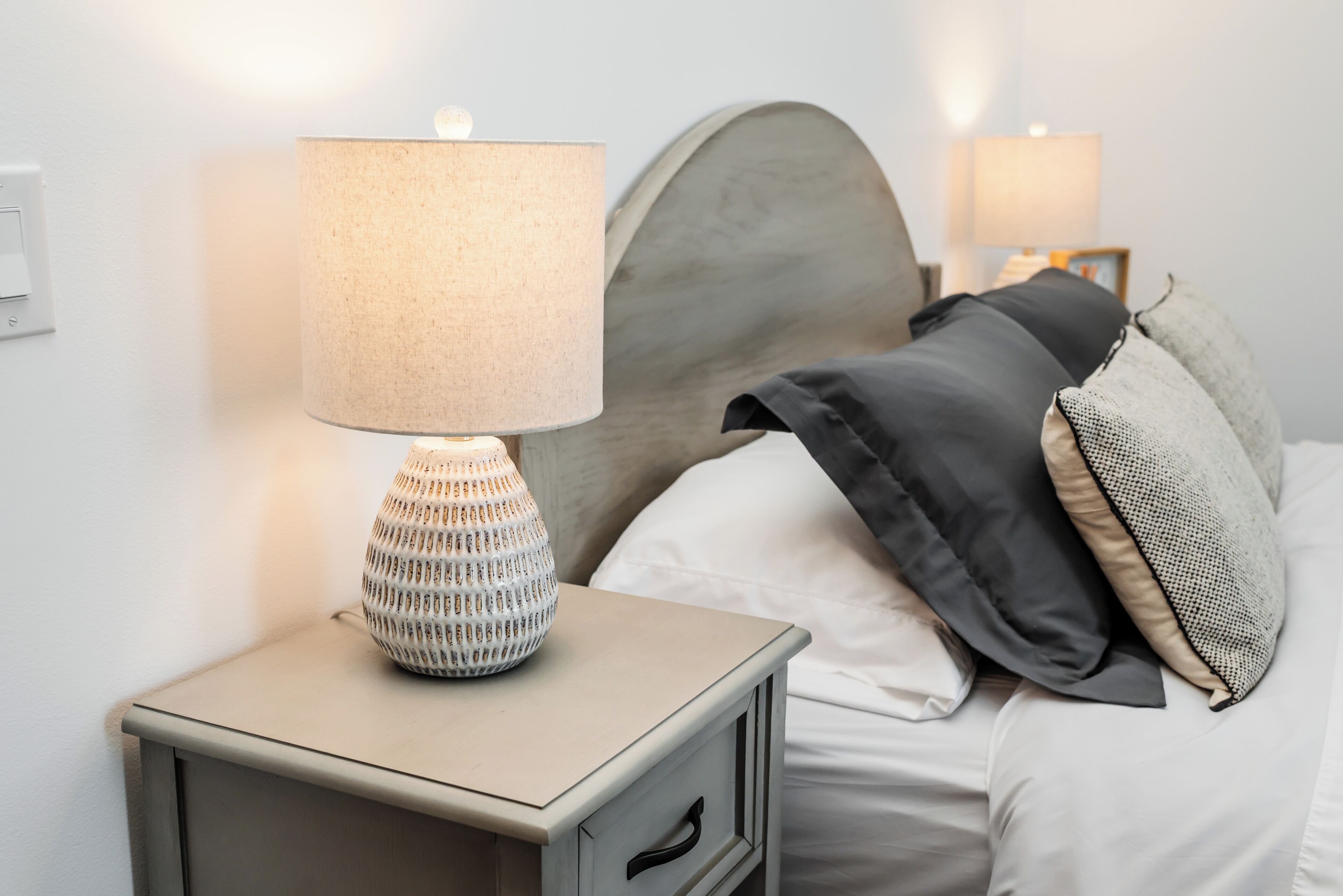 Un lit bien fait, avec une tête de lit, une lampe de chevet et une table de chevet dotée d’un tiroir.