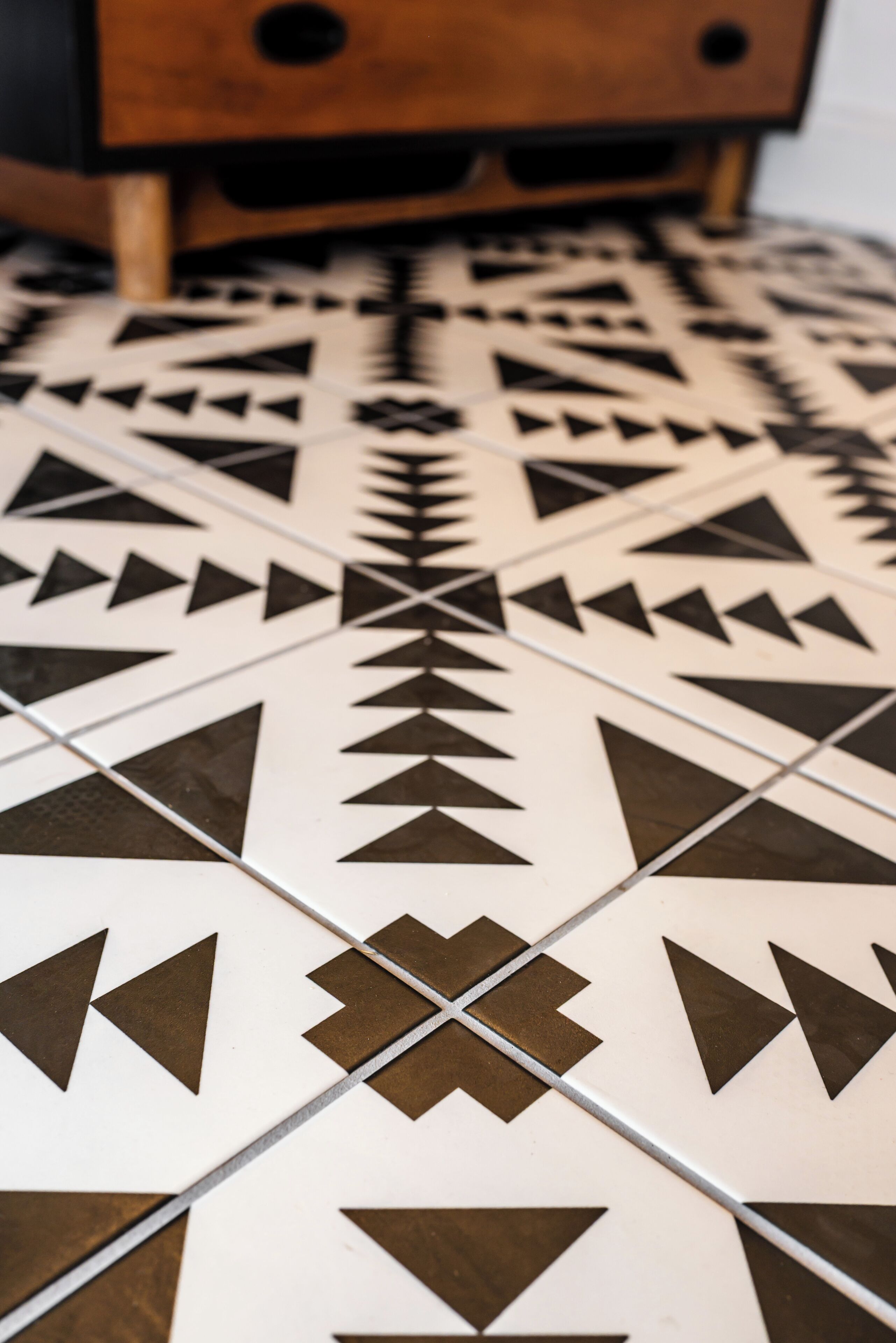 A patterned floor with geometric shapes and a wooden piece of furniture in the background.