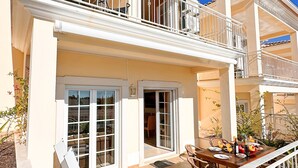 En toetages bygning med balkon, terrasse med udendørs møbler, og en skydedør, der fører til et indvendigt rum.