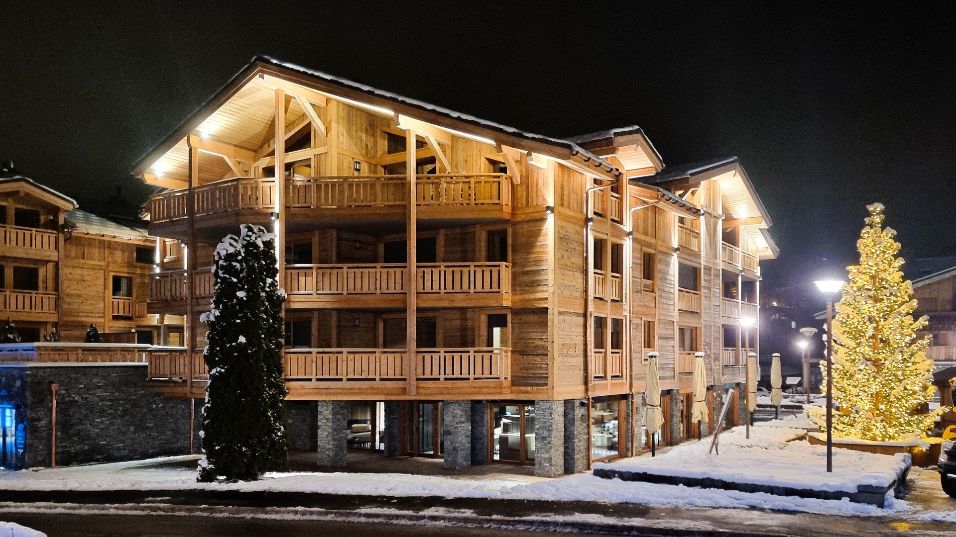 Un bâtiment en bois à plusieurs étages, doté de balcons, d’une fondation en pierre et d’un sol recouvert de neige.