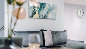 Een moderne woonkamer met een grijze bank, een glazen salontafel en een abstract schilderij dat aan de muur hangt.