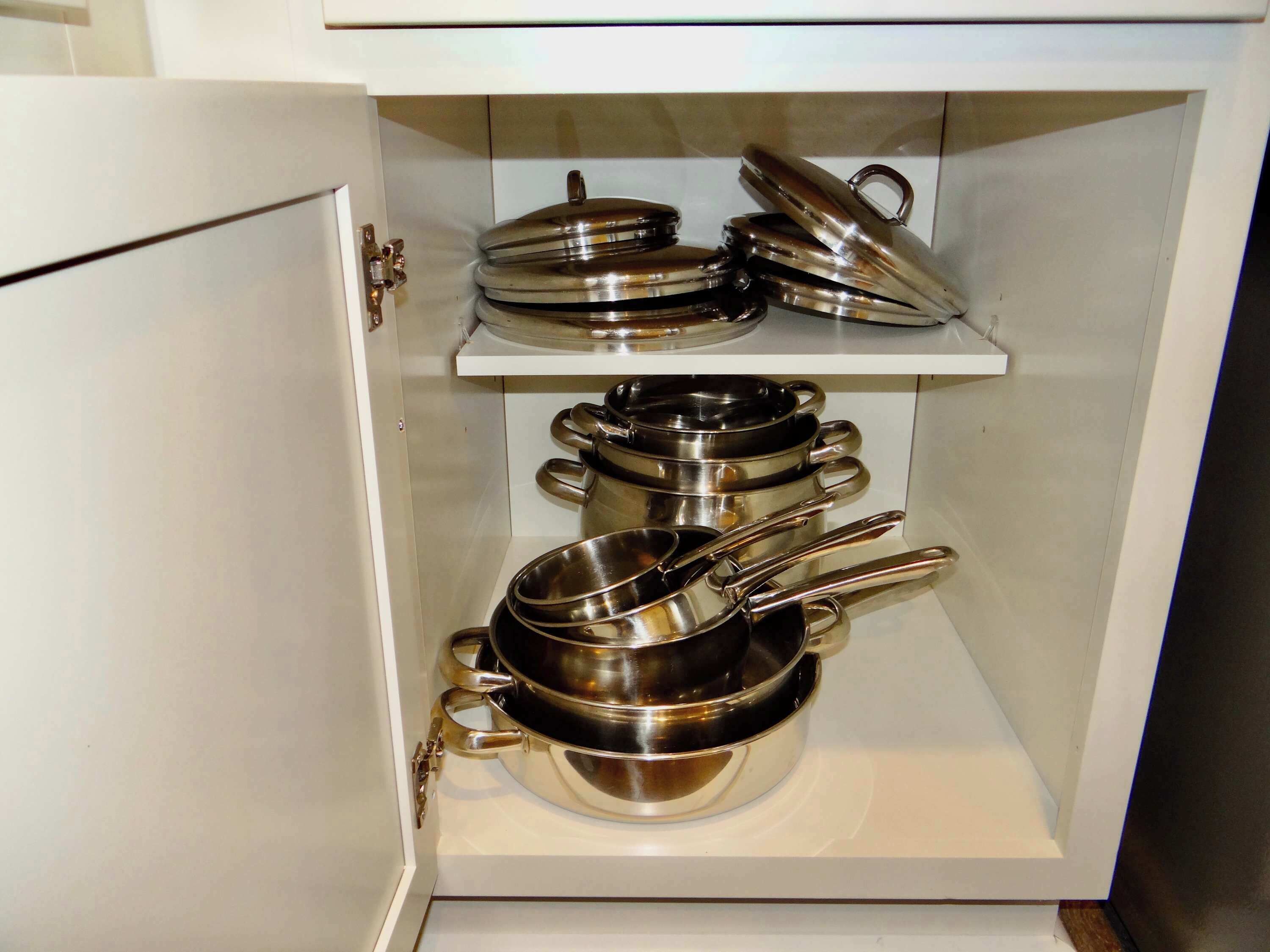 Un armario de cocina con utensilios de acero inoxidable, incluyendo ollas y sartenes, ordenados en estantes.