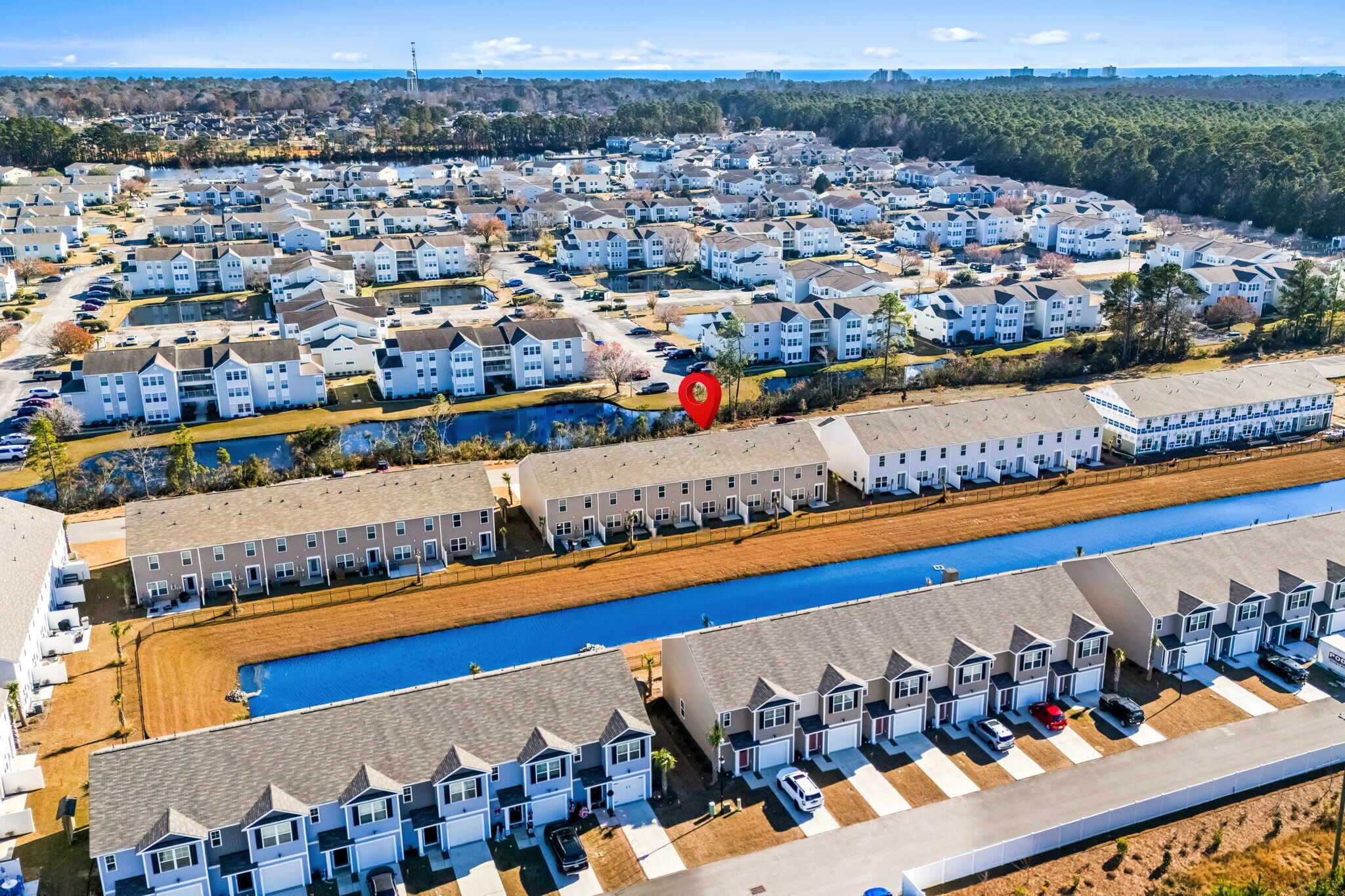 An aerial view of a residential area with multiple apartment buildings, a central water body, and a parking lot.