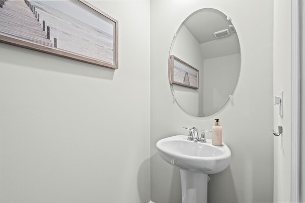 A bathroom with a white sink, a mirror, and a framed picture on the wall. - Birdie Beach House (By Beach Star) (Surfside Beach)