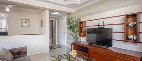 A living room with a sofa, glass coffee table, wooden entertainment unit, and a television.