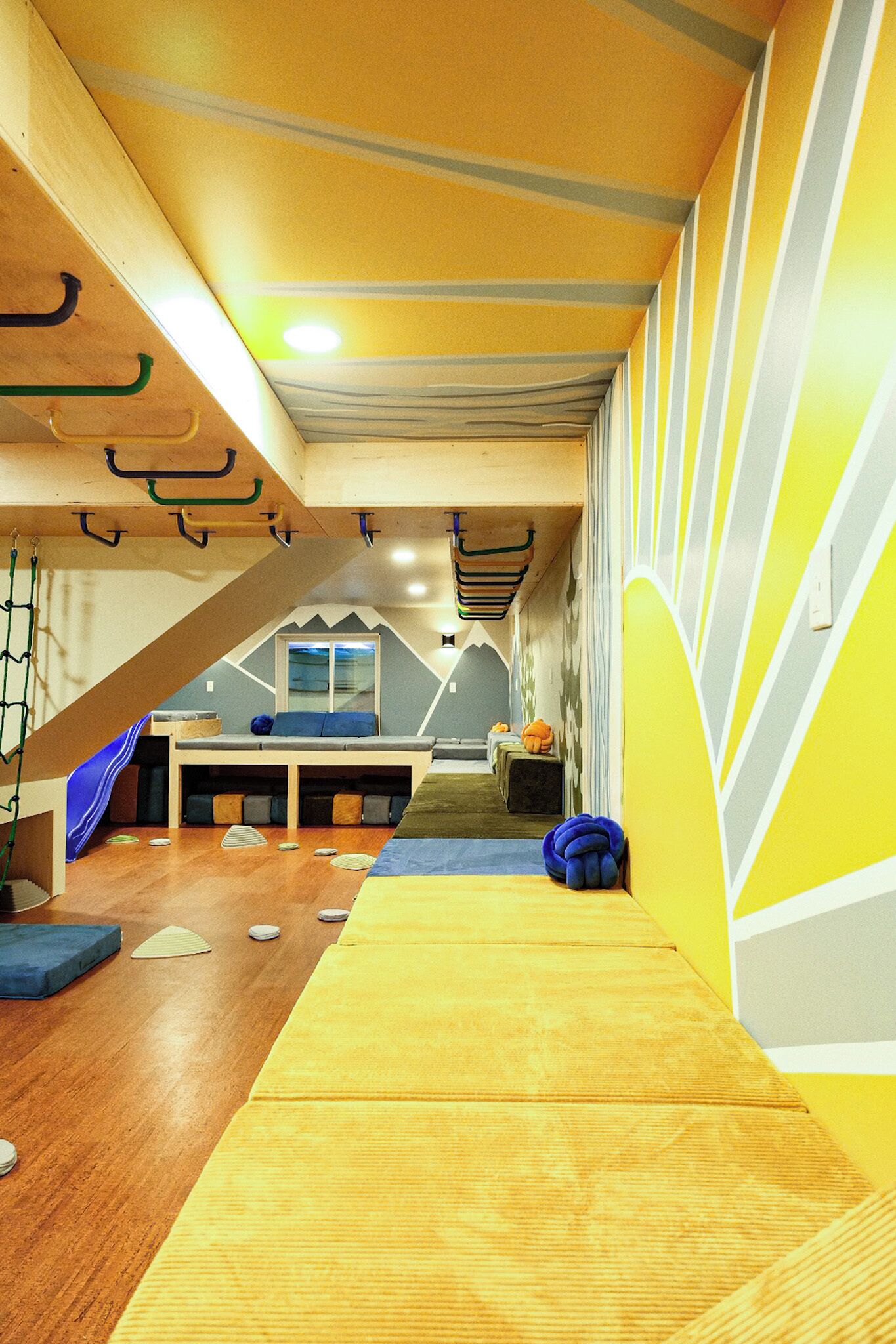 A playroom with a wooden floor, climbing wall, and colorful play mats.