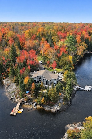 Un chalet au bord du lac, doté d’un quai, entouré d’un paysage automnal aux couleurs flamboyantes.