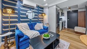 Una sala de estar moderna con un sofá azul, una mesa de centro negra y una cocina visible a través de una puerta abierta.