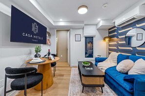 A modern living room with a blue sofa, a wooden dining table, and a mounted TV displaying 'CASA HOTELS TORONTO'. - The McCaul | Basement Suite Near Chinatown (Toronto)