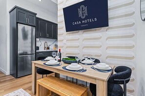 A modern kitchen with dark cabinets, a stainless steel refrigerator, and a dining area with a wooden table set for four.