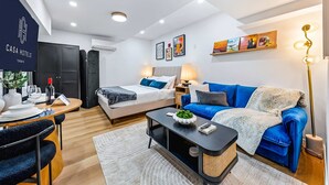 Ein modernes Hotelzimmer mit einem Bett, einem blauen Sofa, einem Esstisch und einem Couchtisch.