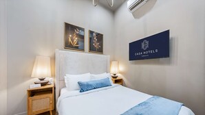 Hotellihuone, jossa on sänky, kaksi yöpöytää valaisimineen, seinälle asennettu televisio ja kaksi kehystettyä kukka-aiheista taideteosta.