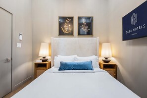 Habitación de hotel con cama, dos lámparas de noche, un cartel en la pared y dos cuadros enmarcados.