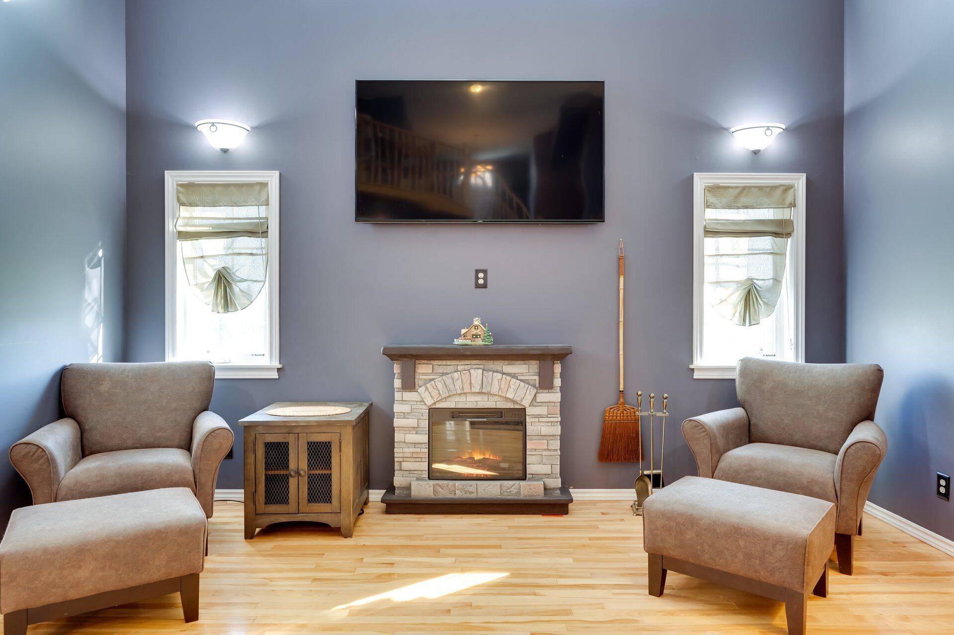 A living room with two armchairs, a small side table, a fireplace, and a television mounted on the wall.