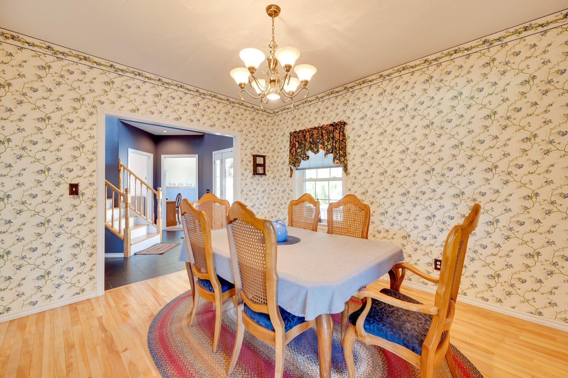 A dining room with a chandelier, floral wallpaper, and wooden chairs.