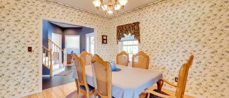 A dining room with a chandelier, floral wallpaper, and wooden chairs.