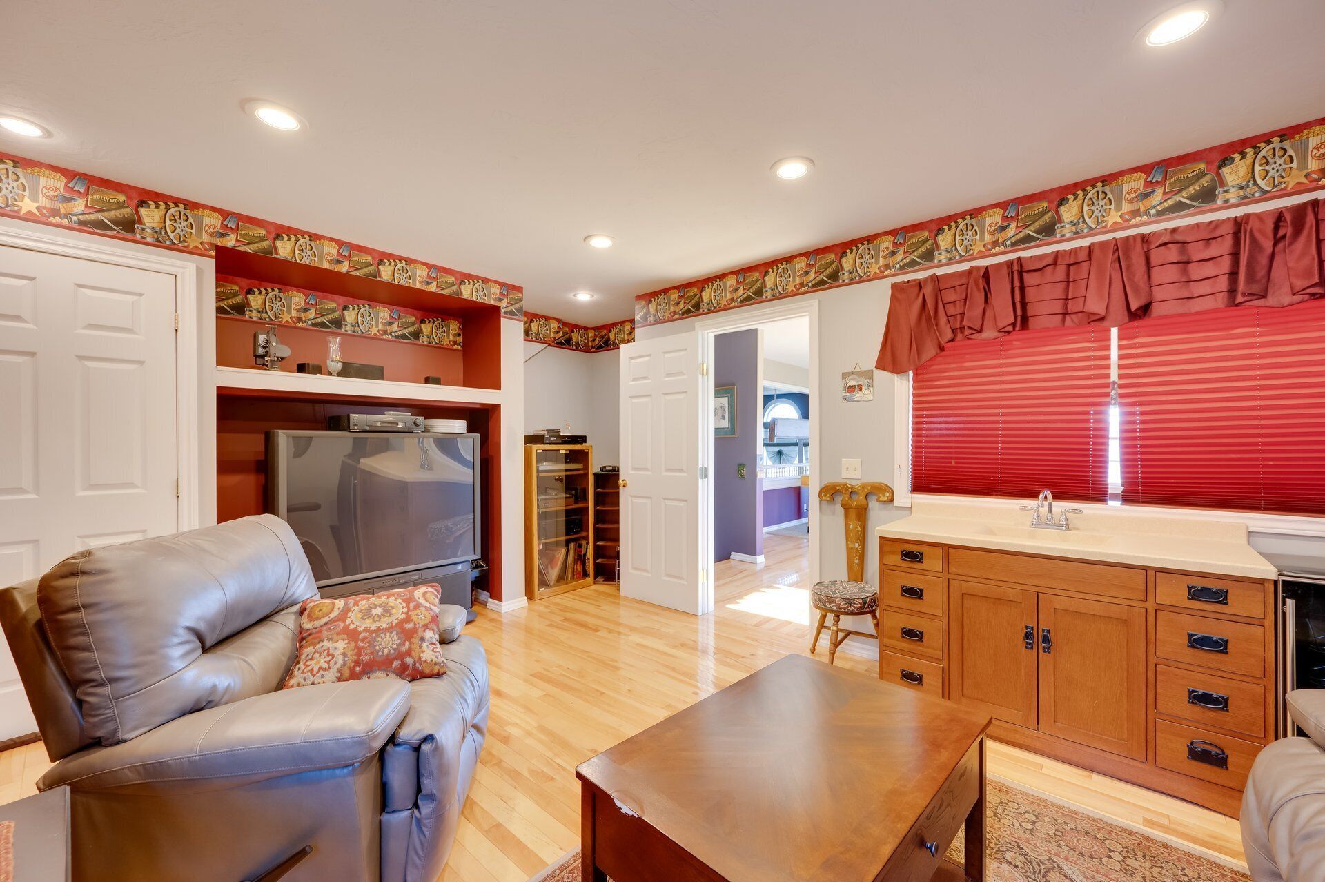 A living room with a leather sofa, a wooden coffee table, and a TV. There is a kitchen area with a sink and cabinets.