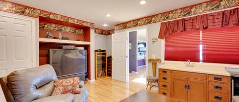 A living room with a leather sofa, a wooden coffee table, and a TV. There is a kitchen area with a sink and cabinets.