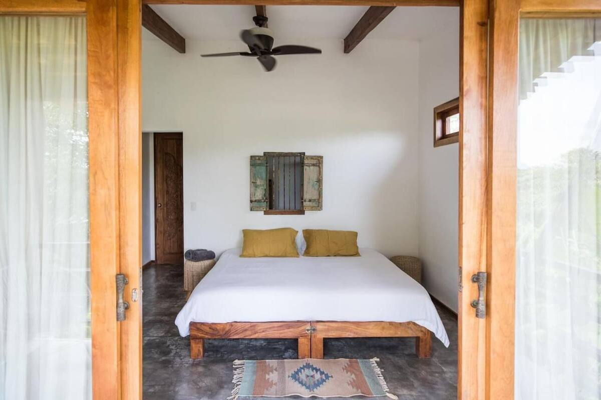 A bedroom with a bed, wooden headboard, a ceiling fan, a window, and a door.
