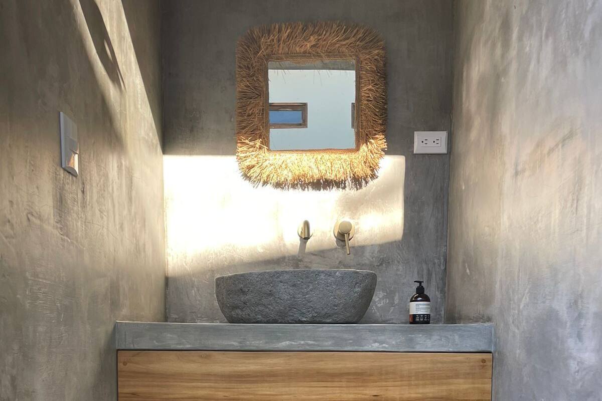 A bathroom with a stone sink, wooden vanity, and a mirror with a textured frame.